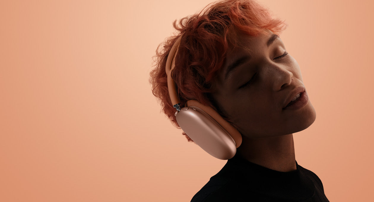 A person wearing orange AirPods Max 2 over an orange-pink background.